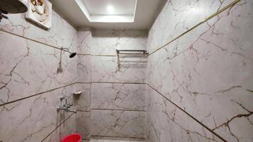 A bathroom with marble walls, a shower, a red bucket, and a ceiling light.