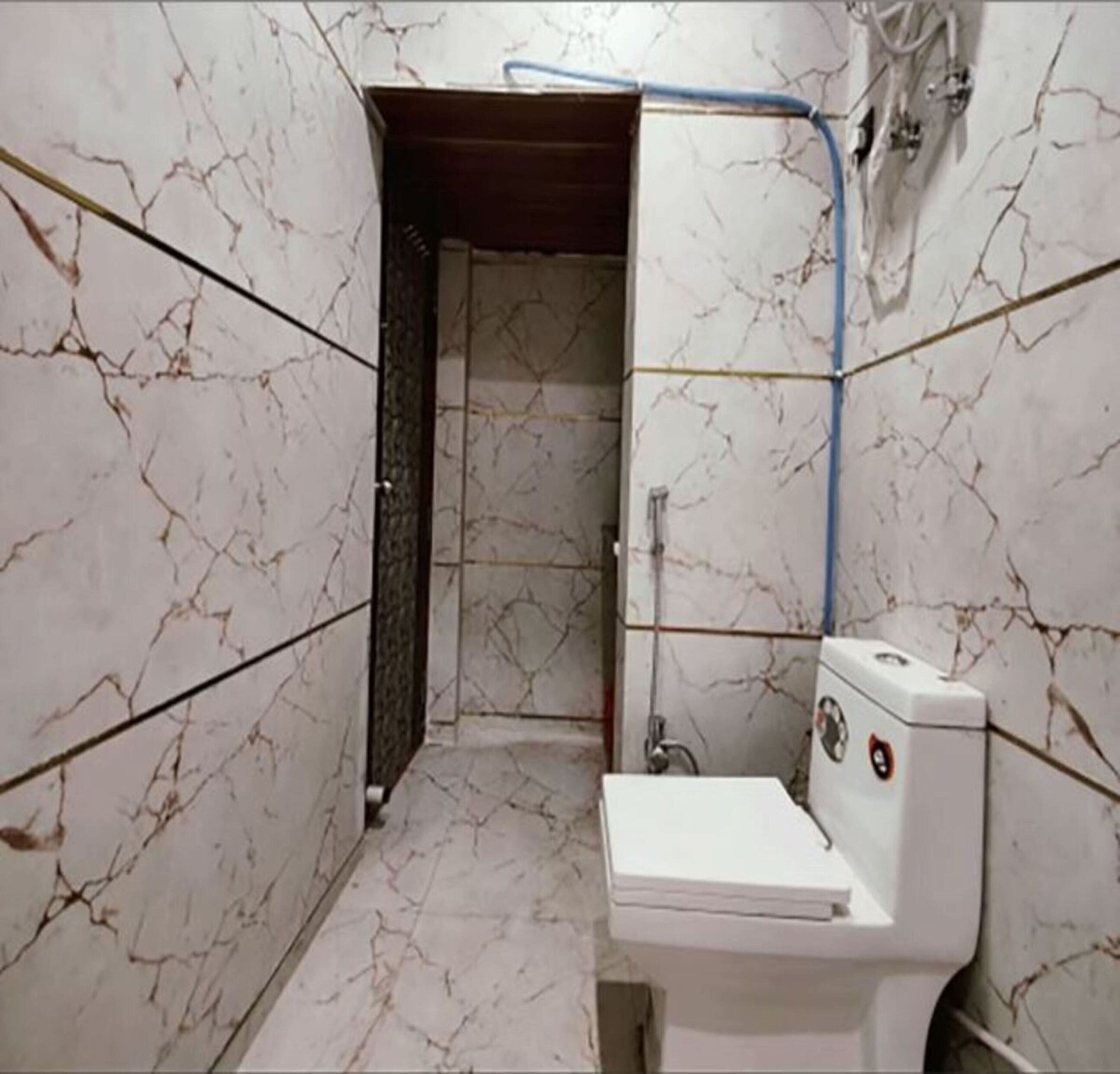 A bathroom with a toilet, a shower, and a marble-patterned wall.