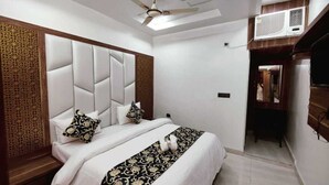 A bedroom with a large bed, a ceiling fan, an air conditioning unit, and a wooden panel on the wall. - Hotel Royal Vrindavan (Aligarh)