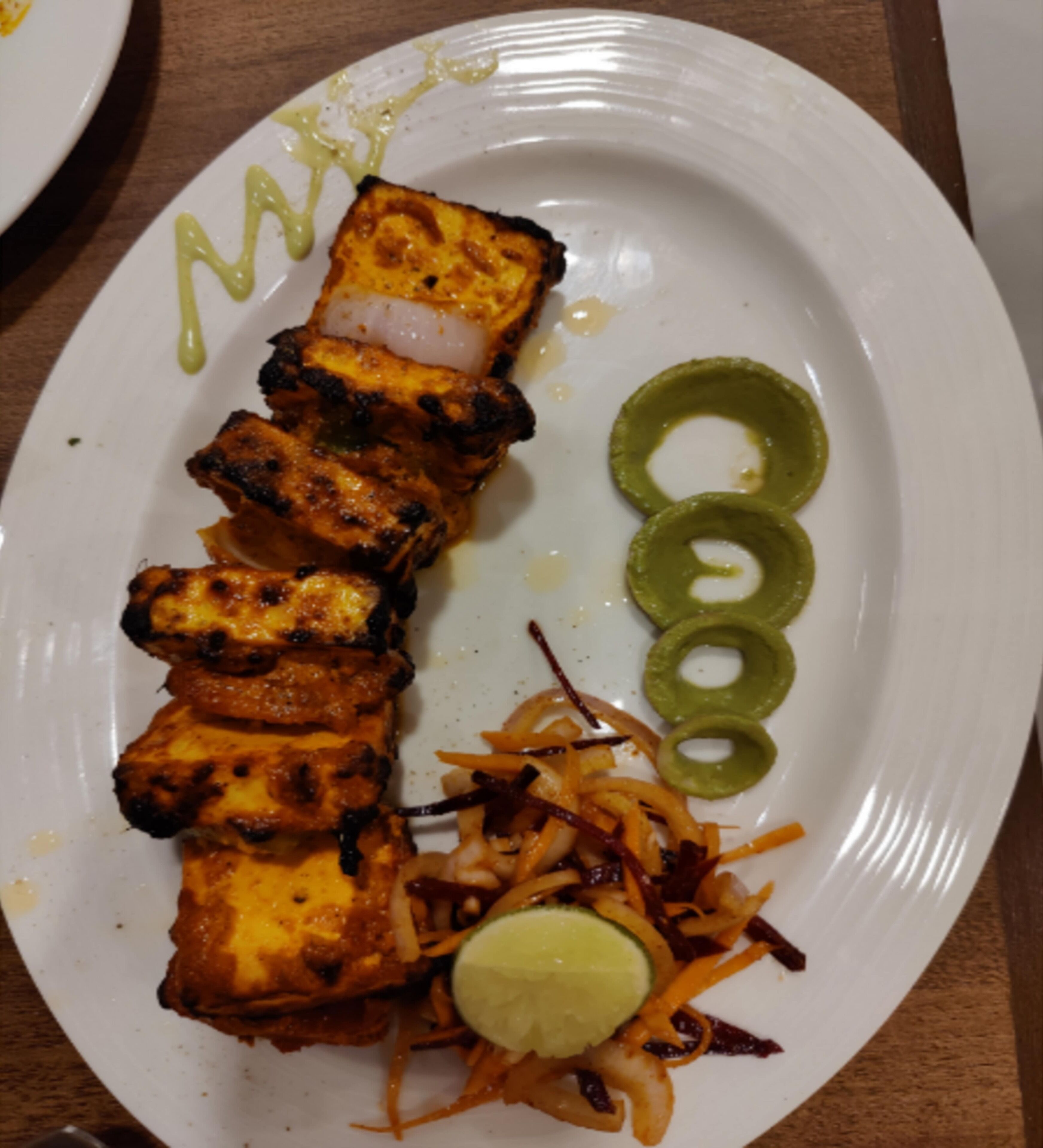 A plate with grilled paneer, sliced onions, carrot slaw, and lime wedges.