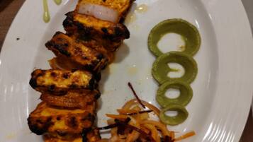 Un plato con paneer a la parrilla, cebollas en rodajas, ensalada de zanahoria y gajos de lima.