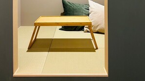 A minimalist room with a low wooden bed frame, a tatami mat floor, and a simple wooden bench. - Hotel Kanma Ueno (Tokyo)