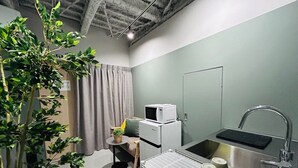 A compact kitchen with a microwave, sink, and small table with a plant. - Hotel Kanma Ueno (Tokyo)