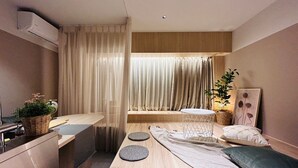 A modern, minimalist room with a wooden floor, a small round table, a sofa, and a window with sheer curtains. - Hotel Kanma Ueno (Tokyo)
