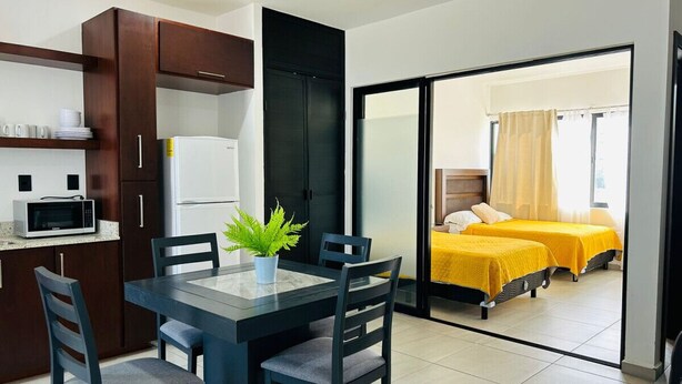 Quarto de hotel compacto com área de refeições, cozinha compacta e varanda com duas camas.