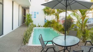 Uma área de piscina com mesa e cadeiras, cercada por plantas e um portão.