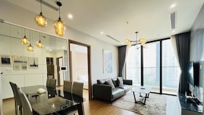 A modern living room with a glass dining table, leather sofa, and a large TV. - Vinhomes Skylake - SunhouseLand (Hanoi)