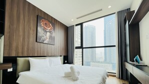 A modern hotel room with a large bed, a wooden accent wall, a city view, and a painting. - Vinhomes Skylake - SunhouseLand (Hanoi)