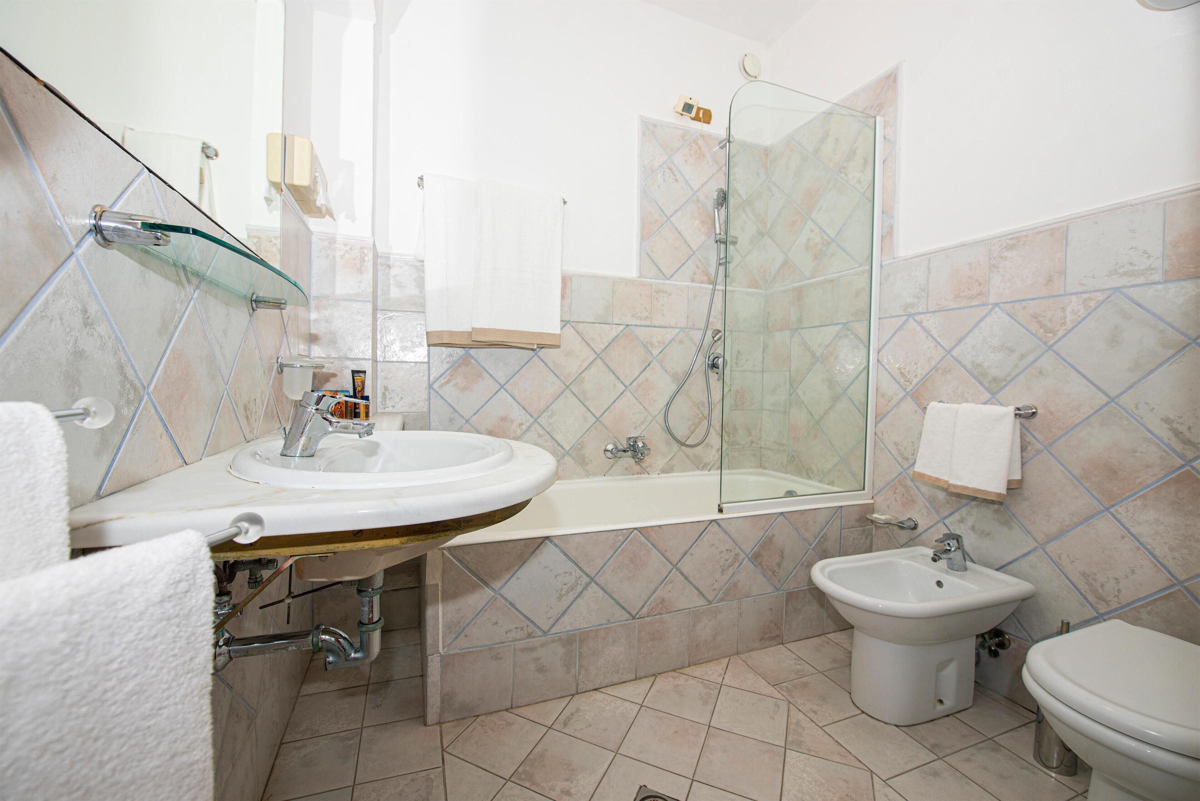 A bathroom with a glass shower enclosure, a sink, a bidet, and a toilet.