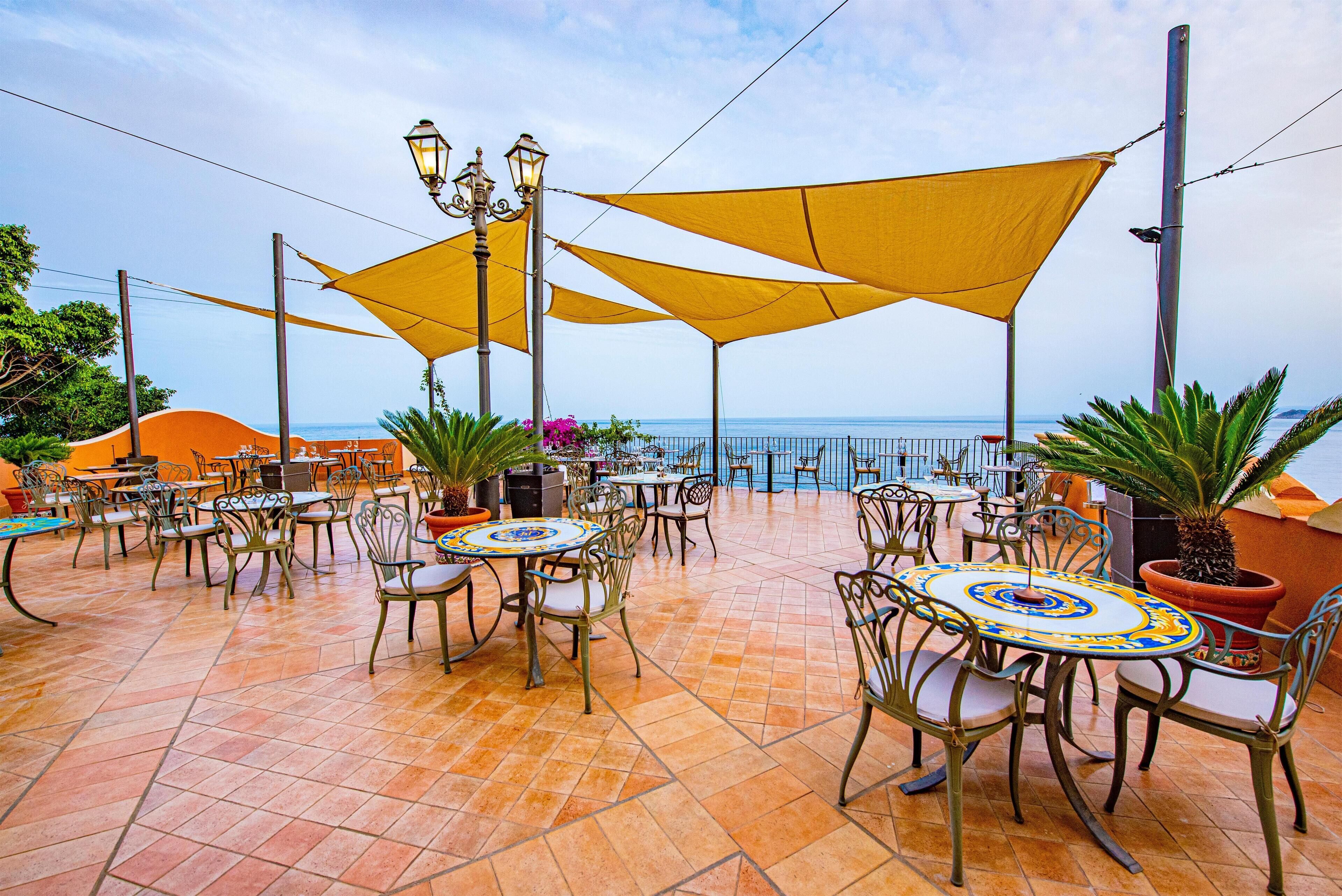 An outdoor patio with tables and chairs, yellow canopies, and a view of the sea.