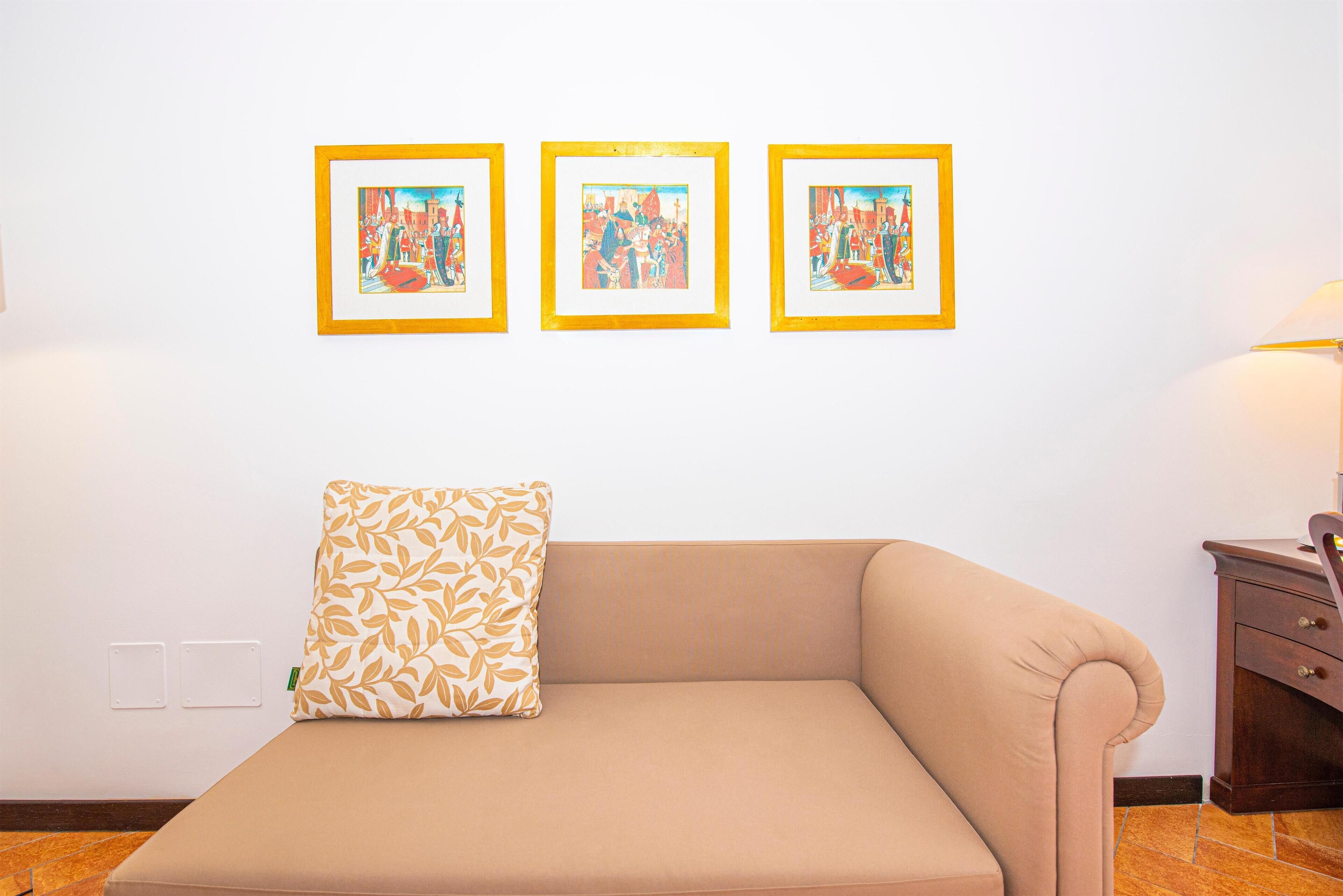 Een kamer met een beige bank, een kussen met dessin en drie ingelijste kunstwerken aan de muur.
