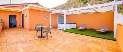 A patio with a table and chairs, a hot tub, and a covered seating area with a view of a mountainous landscape.