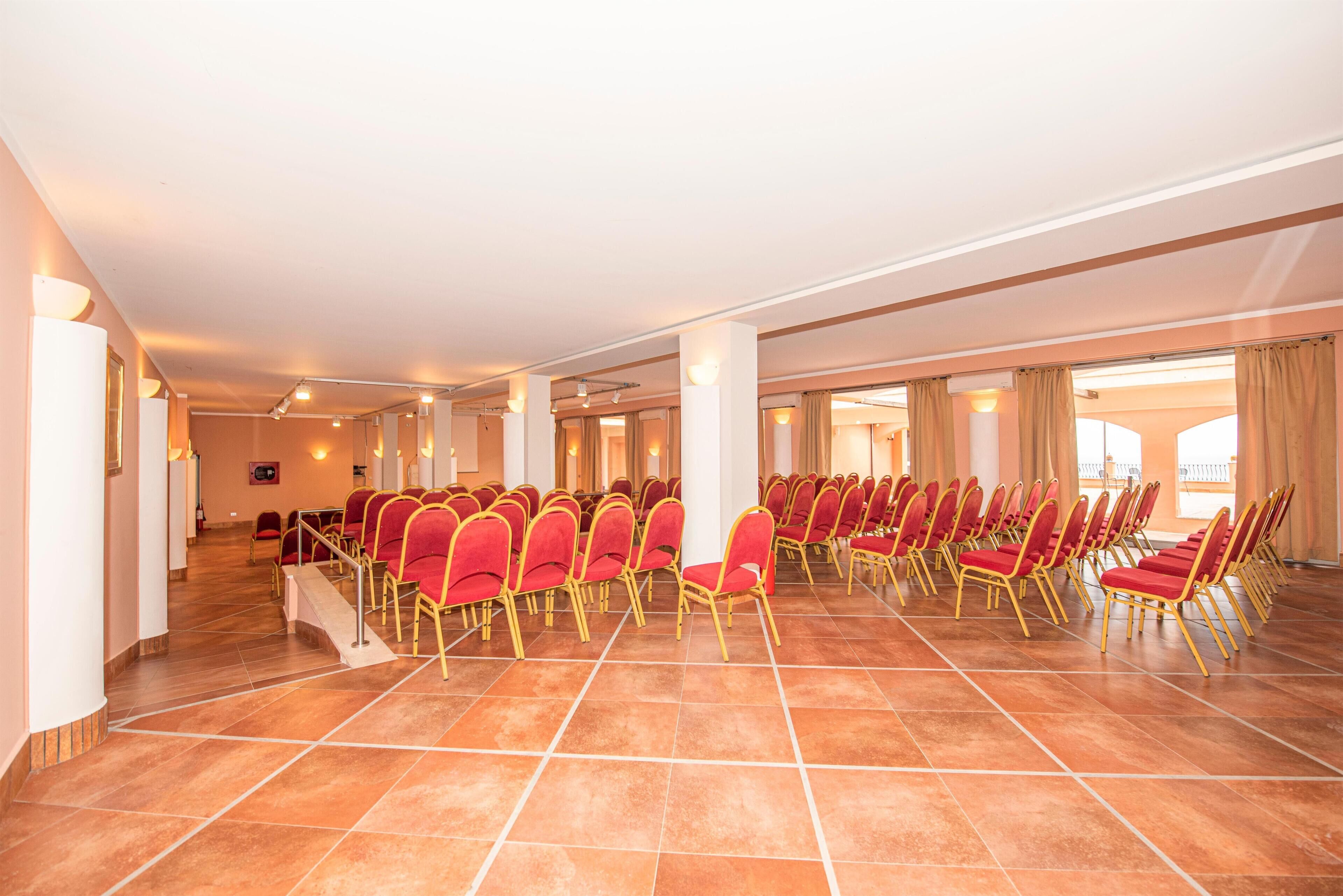 Una amplia sala de conferencias con hileras de sillas rojas y piso de baldosas.