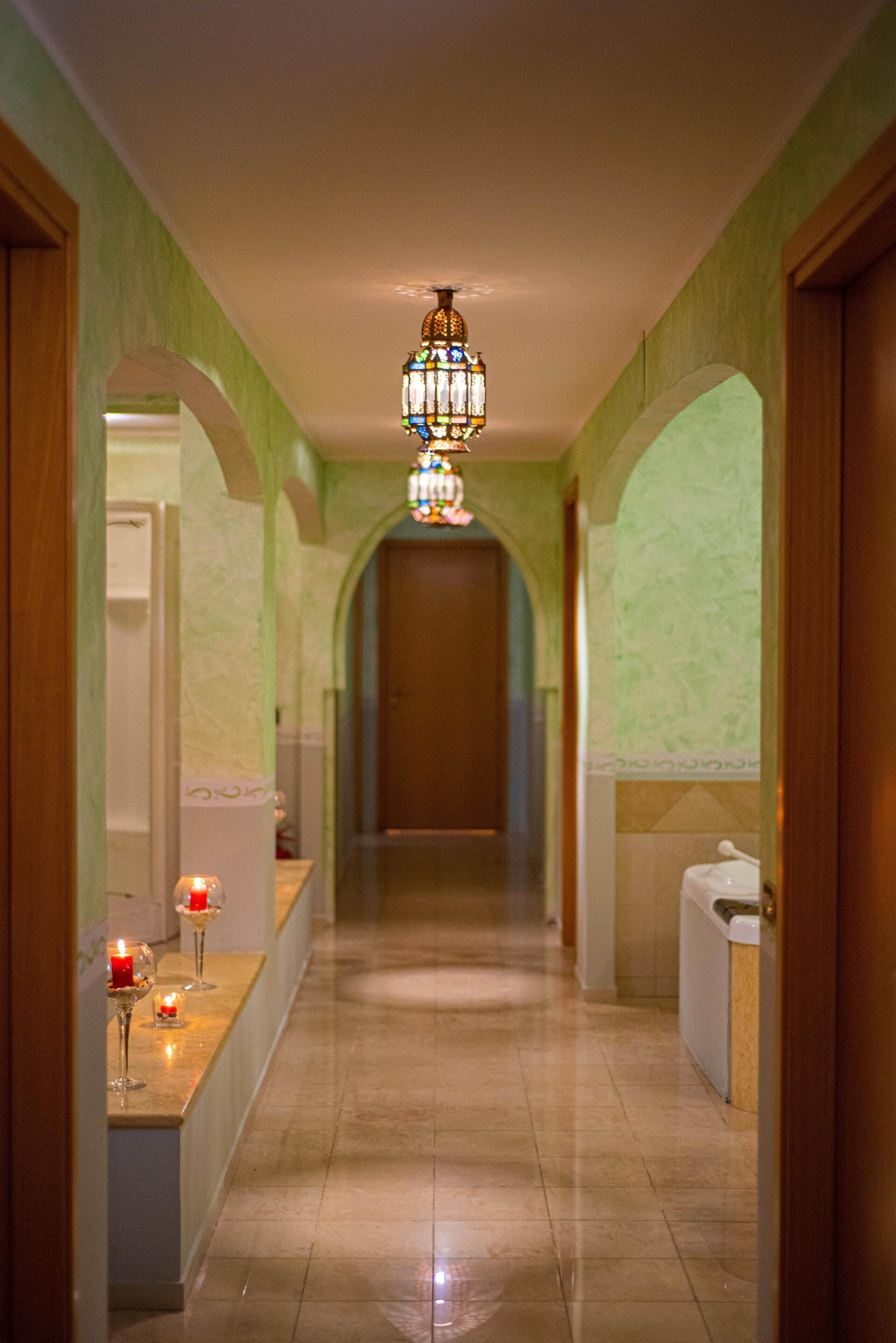 A corridor with a chandelier, a reception desk with candles, and a door at the end.