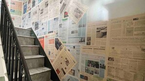 Un escalier avec une rampe en métal, entouré de murs recouverts de journaux.