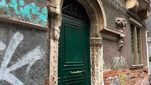 Une porte verte avec un portail en métal, une arche en pierre et un mur de briques orné de quelques graffitis.