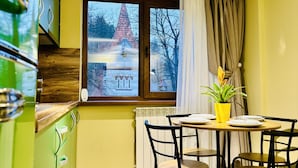 A dining area with a table set for two, a window with a view of a building, and a green cabinet with a radiator below.