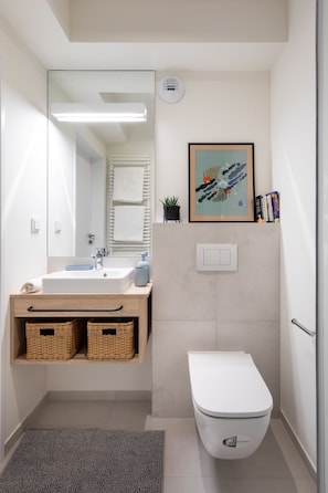 A modern bathroom with a white sink, mirror, and toilet. There are wicker baskets under the sink and a framed picture above the toilet. - MILESTONE Krakow Center Student Living by Tribera (Kraków)