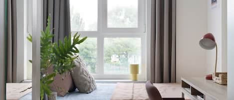 Una habitación con cama, escritorio, silla, ventana con cortinas y una planta.