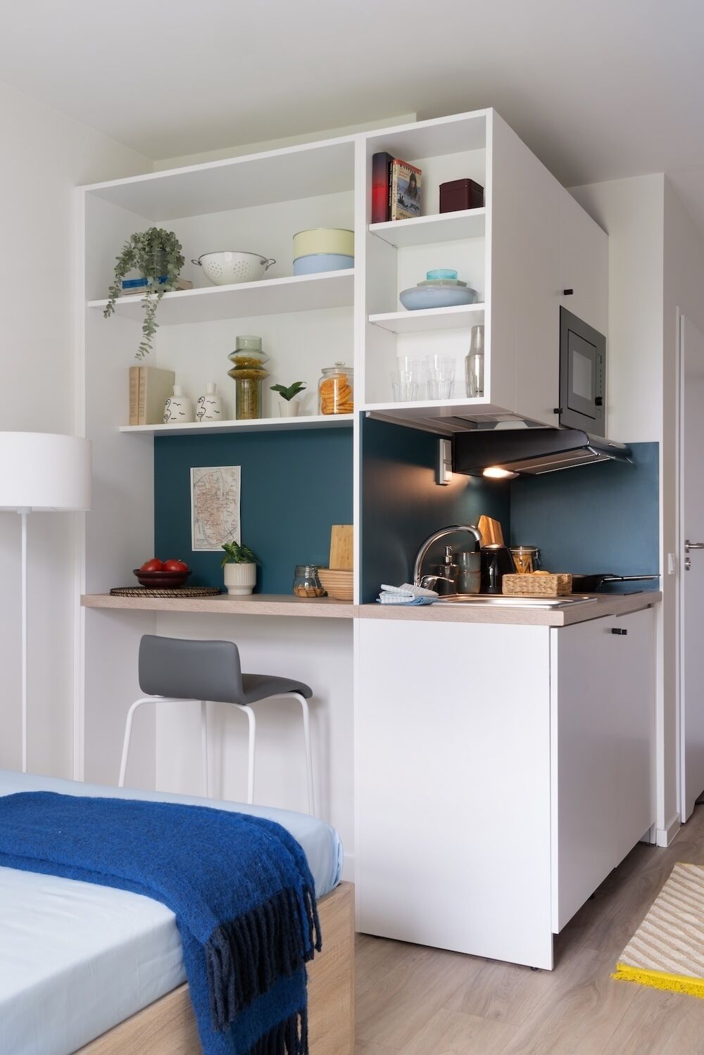 A compact kitchenette with a microwave, stove, and shelves with kitchenware.