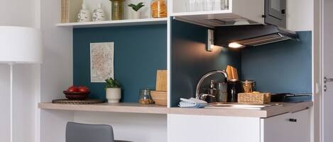 A compact kitchenette with a microwave, stove, and shelves with kitchenware.