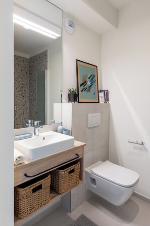 A modern bathroom with a white sink, mirror, and toilet. There are wicker baskets under the sink and a framed picture on the wall. - MILESTONE Krakow Center Student Living by Tribera (Kraków)
