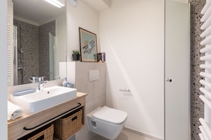 A modern bathroom with a white sink, a toilet, and a shower. There is a framed artwork above the sink and a towel rack on the wall. - MILESTONE Krakow Center Student Living by Tribera (Kraków)