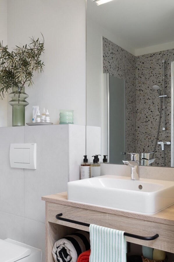 Un baño moderno con un lavabo blanco, un espejo, una ducha y un perchero para toallas.