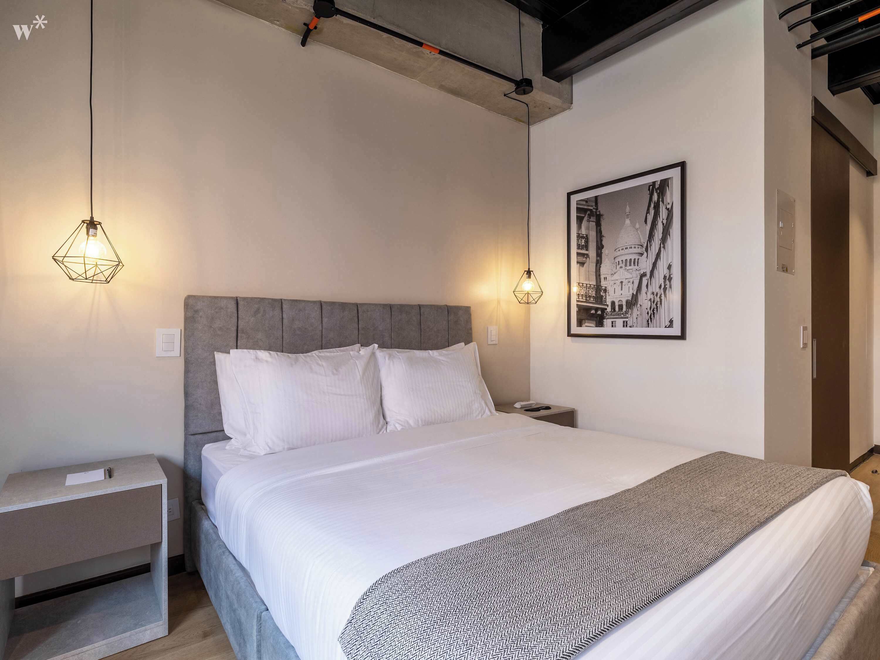 A modern bedroom with a large bed, a grey headboard, two bedside tables, and a framed picture on the wall.