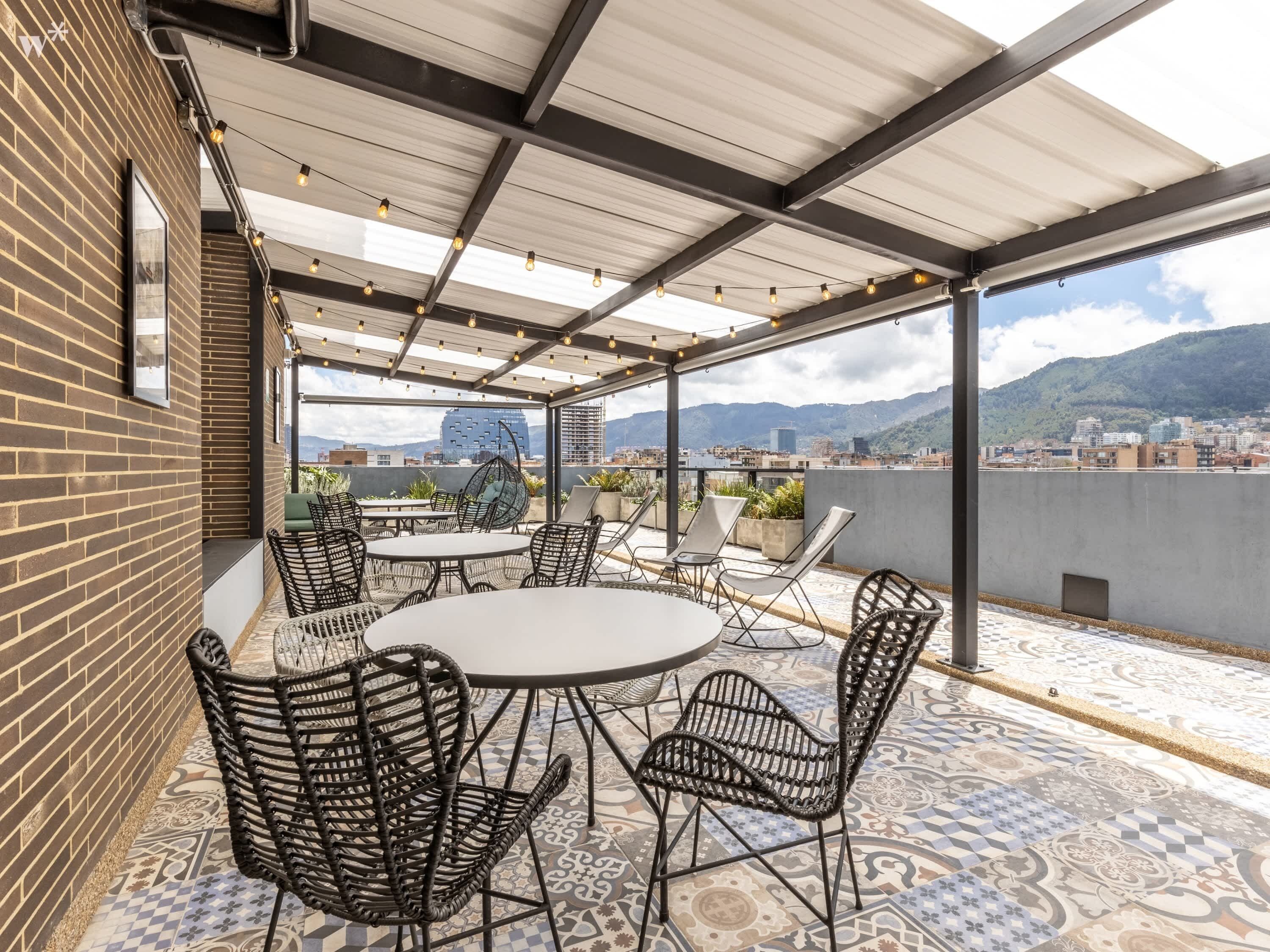 A covered outdoor seating area with a city view, featuring a round table and wicker chairs.