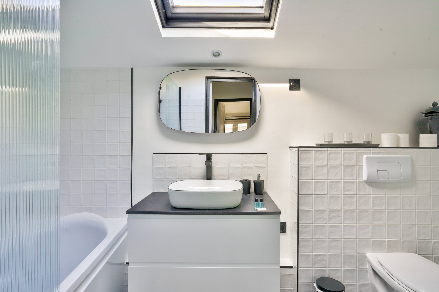 A modern bathroom with a skylight, a round mirror, a white sink, and a bathtub.
