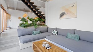 Uma sala de estar moderna com um sofá seccional cinza, uma mesa de centro de madeira e uma escada com luminária de fibra.