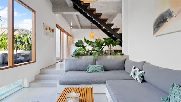 Uma sala de estar moderna com um sofá modular cinzento, uma mesa de centro de madeira e uma escadaria que leva a um andar superior.
