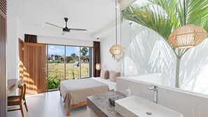 Quarto moderno com uma cama grande, um espaço de estar, um banheiro com uma pia espaçosa e vista para o verde lá fora.