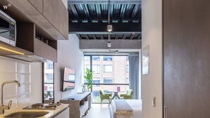 A modern kitchen with a microwave, sink, and stove. There is a dining area with a table and chairs, and a bed with a view of the city. - w * | Cozy Loft in Parque Virrey (Bogotá)