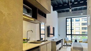A modern kitchen with a built-in microwave, a sink, and a dishwasher. There is a dining area with a table and chairs, and a large window providing a view of the city. - w * | Cozy Loft in Parque Virrey (Bogotá)