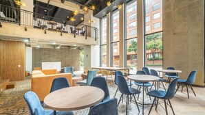 A spacious indoor area with multiple round tables and blue chairs, a wooden bench, and a balcony with outdoor seating.