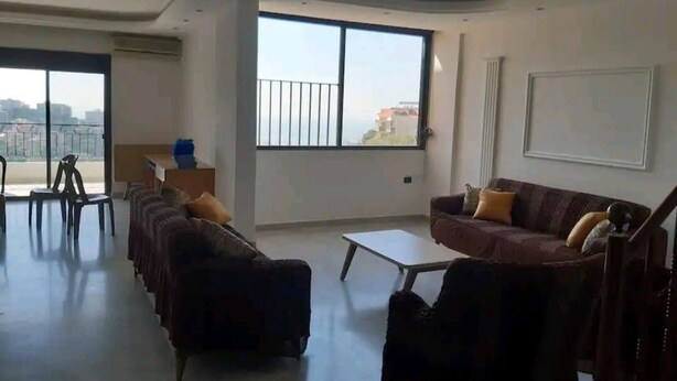 Un salón amplio con un gran ventanal, un sofá, una mesa de centro y un comedor con sillas.
