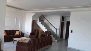 Un salón amplio con un juego de sofá marrón, una mesita de café blanca y un sofá marrón oscuro con cojines. Una escalera conduce a un piso superior.
