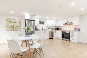 A modern kitchen with white cabinets, stainless steel appliances, and a dining area with white chairs.