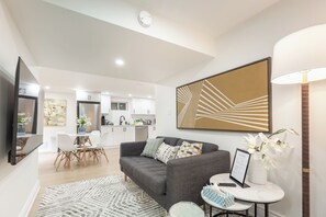 Ein modernes Wohnzimmer mit grauem Sofa, einem Couchtisch und einem Essbereich mit weißem Tisch und Stühlen.