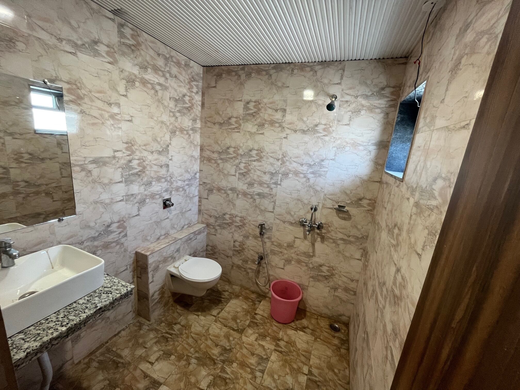 A bathroom with a marble wall, a sink, a toilet, and a shower.