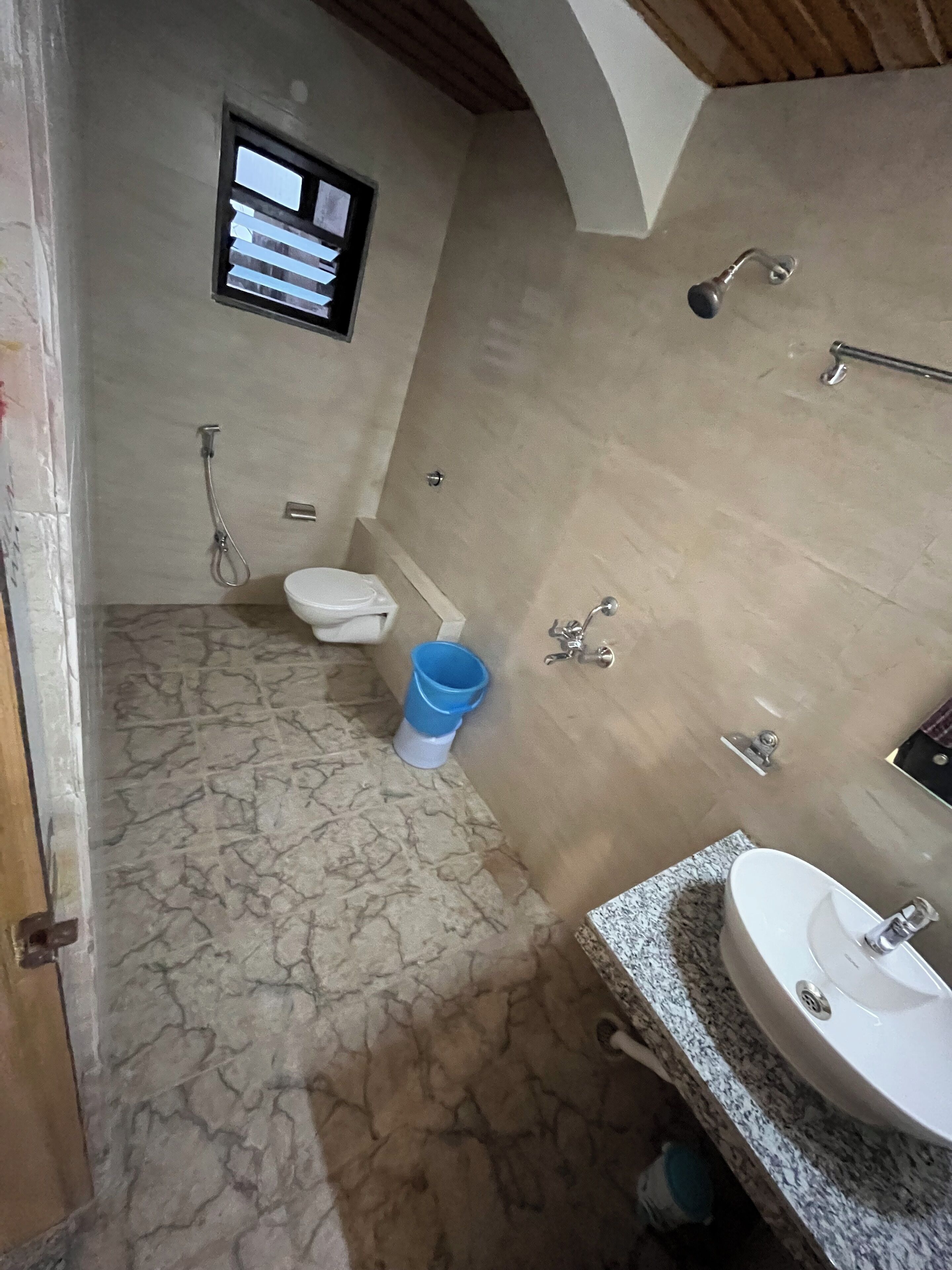 A bathroom with a toilet, a shower, a sink, and a blue bucket.
