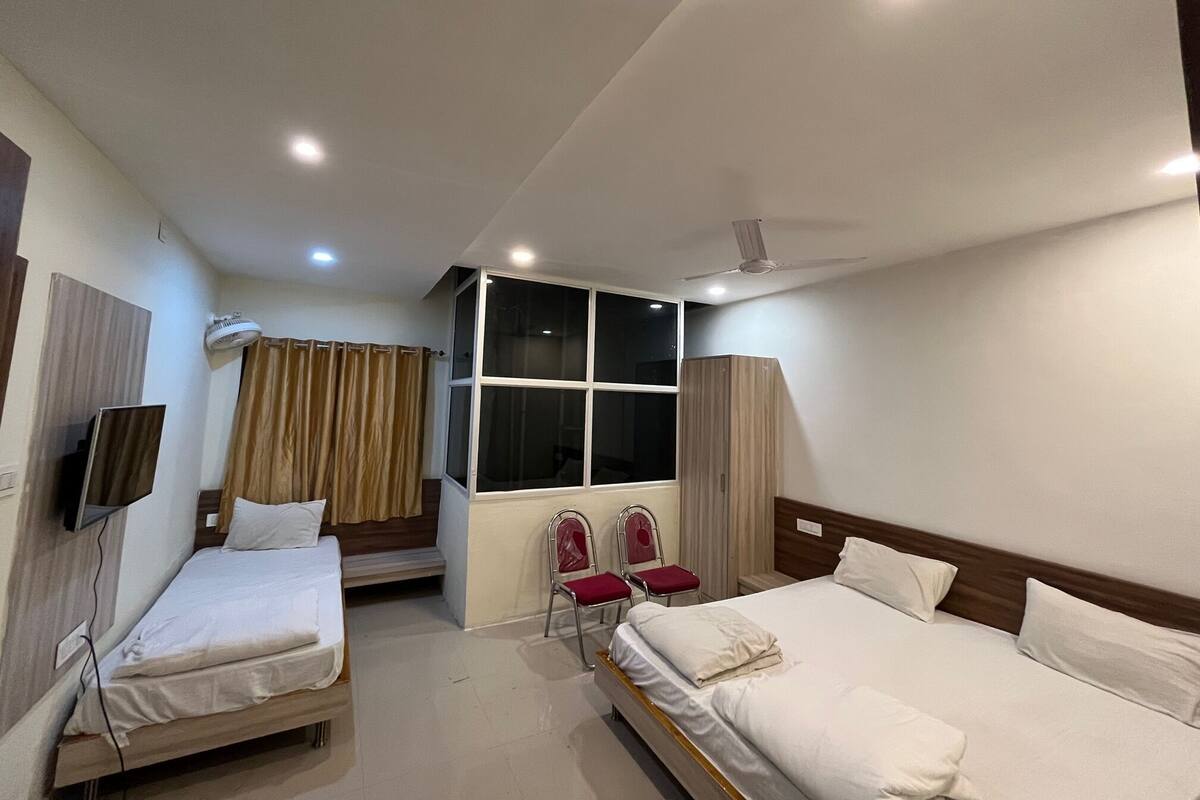 A hotel room with two single beds, a TV, an air conditioning unit, a window with curtains, and a ceiling fan.