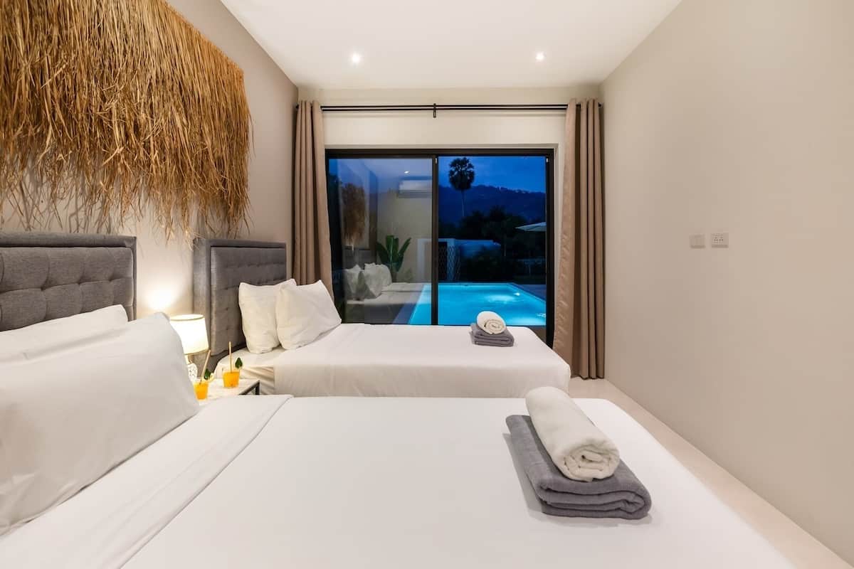 Quarto de hotel moderno com duas camas, uma janela ampla com vista para uma piscina e um painel decorativo na parede.