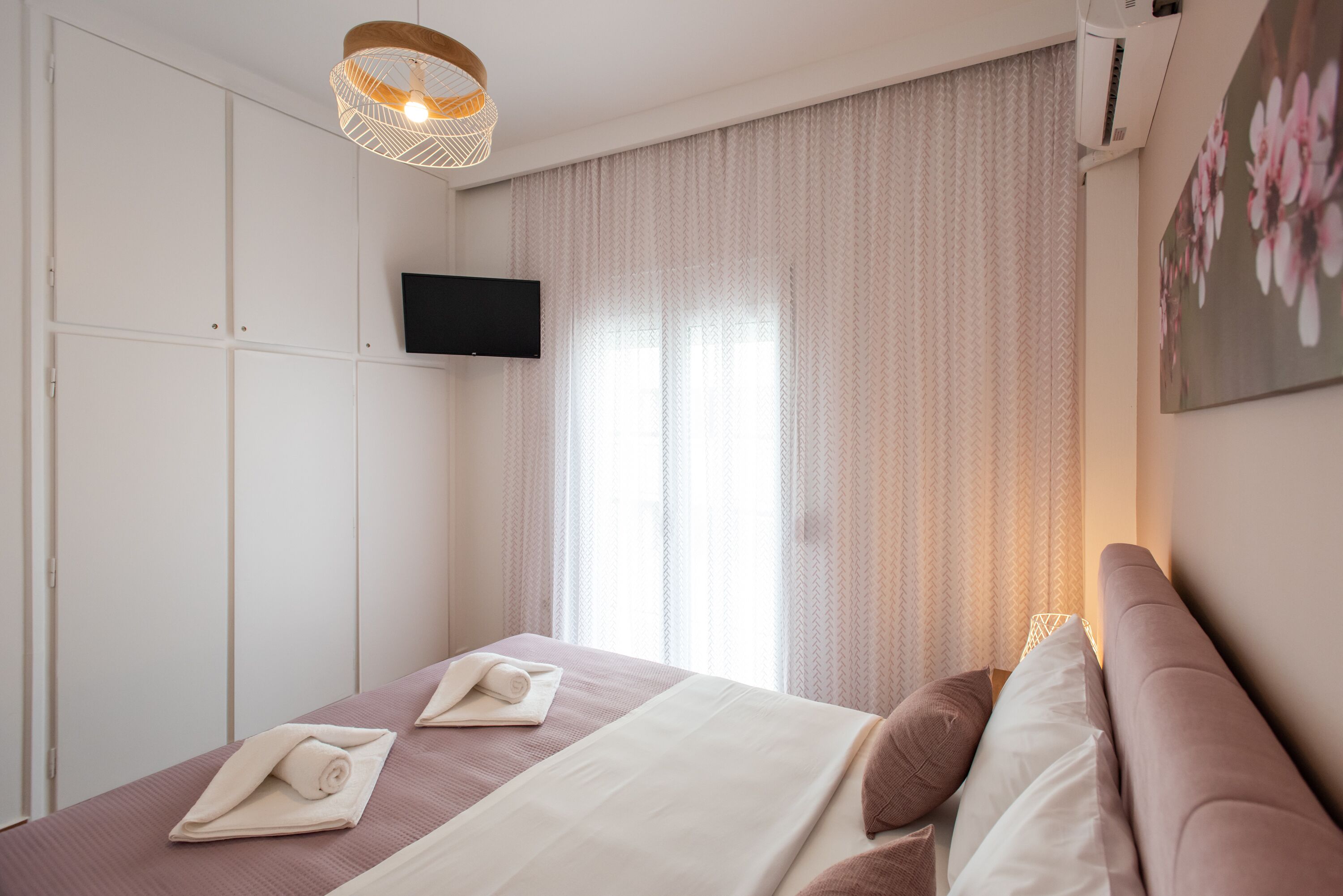 Een hotelkamer met een bed, een aan de muur bevestigde televisie en een raam met gordijnen.