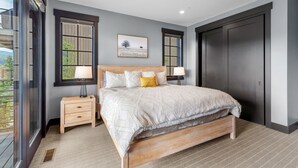 A bedroom with a large bed, two bedside tables, a window, and a door. - Modern Mountain House w/ Private Hot Tub (Big Sky)