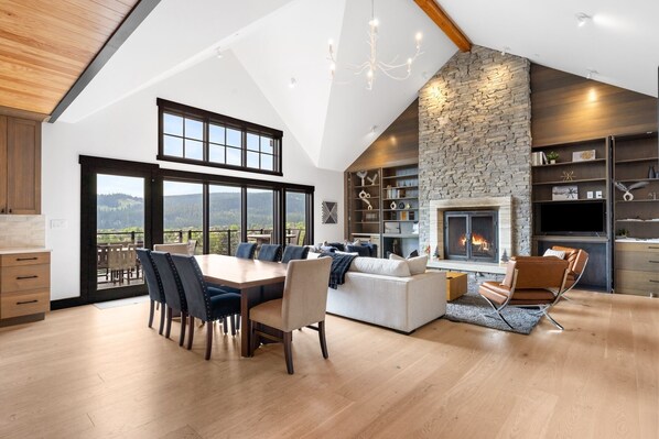 Amplia sala de estar con chimenea, una mesa de comedor con sillas y vistas al exterior.