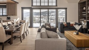 A spacious living room with a large window offering a view of a snowy landscape. - Modern Mountain House w/ Private Hot Tub (Big Sky)