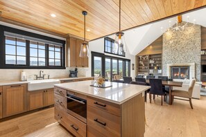 A modern kitchen with wooden cabinets, a large island, and a stone fireplace.
